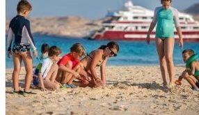 Gyerekek homokoznak egy lakatlan szigeten, háttérben a hajó